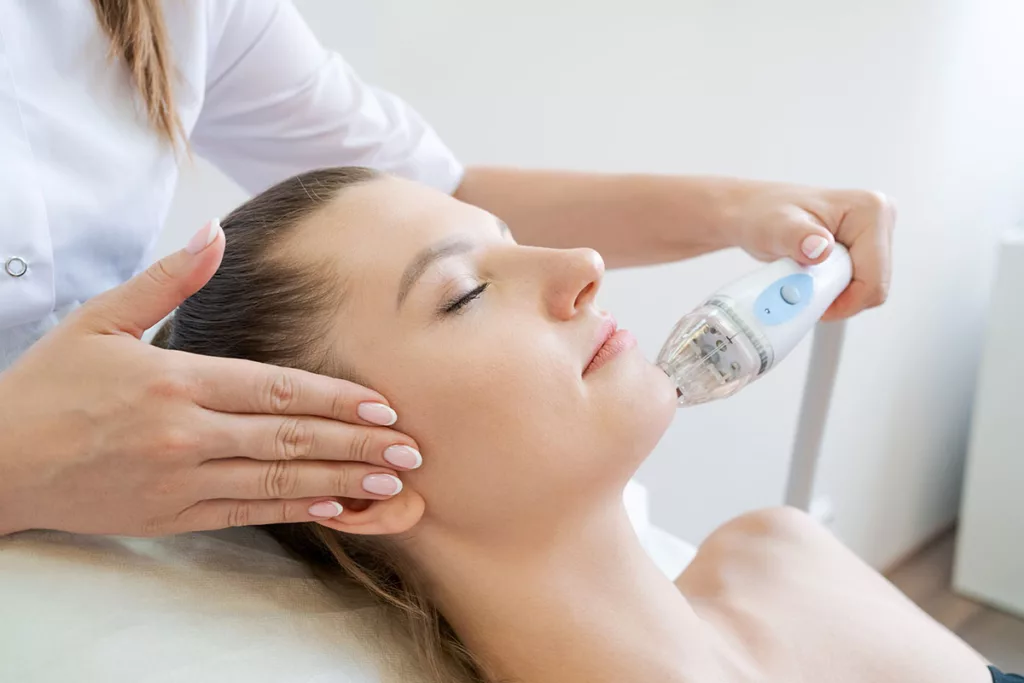 Woman closes her eyes while receiving RF microneedling skin treatment on her face.