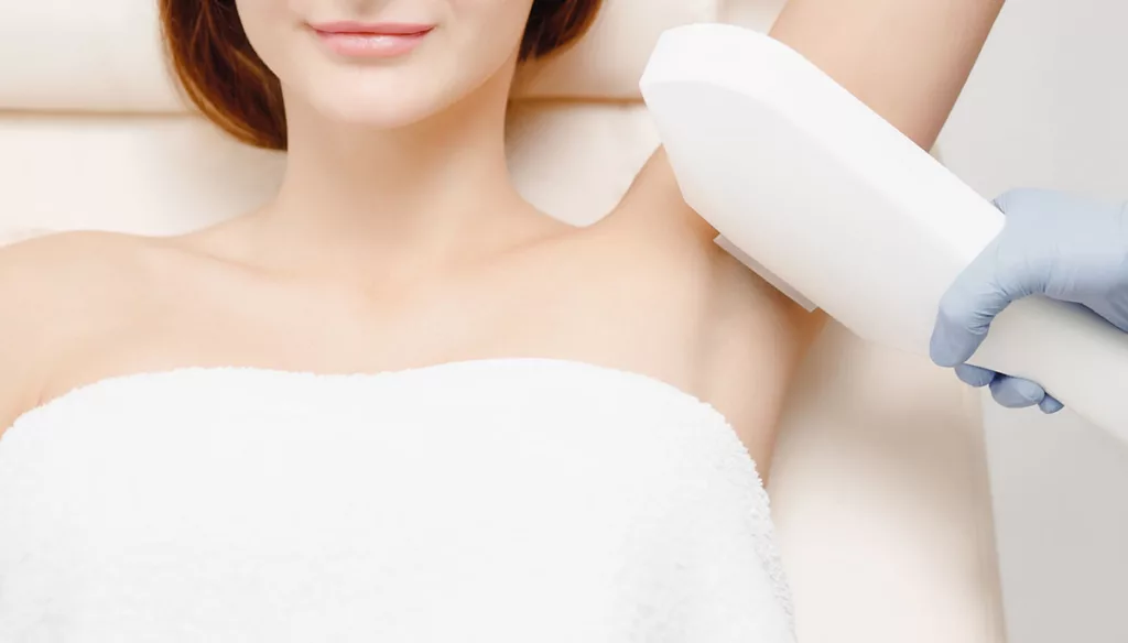 Woman wearing a towel smiles while getting laser hair removal treatment under her arm.