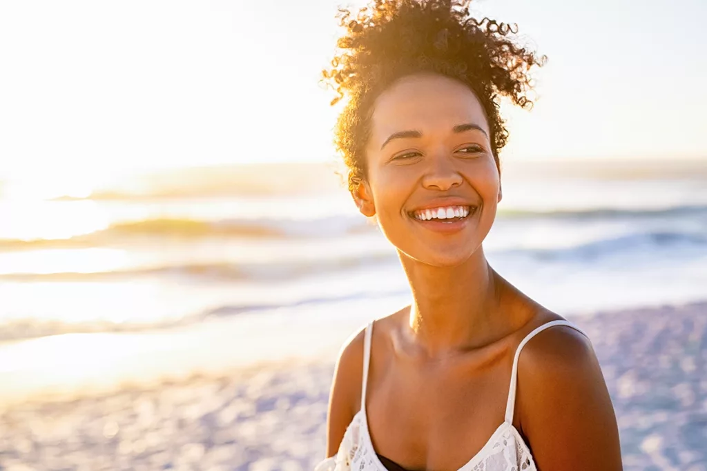 A beautiful young women smiling while walking along the beach during the sunset