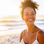 A beautiful young women smiling while walking along the beach during the sunset