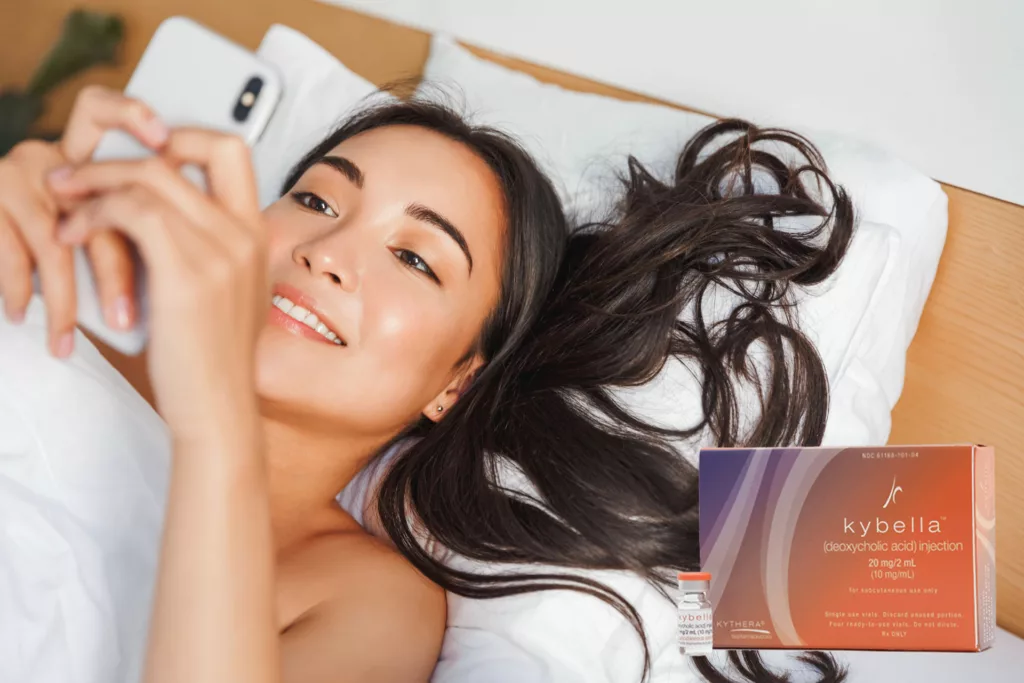 attractive asian woman lounging in bed with her head on a pillow while looking at her smartphone