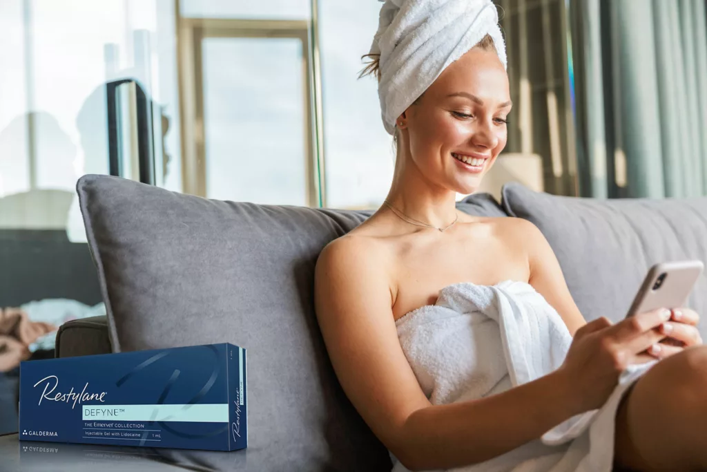 young woman with gorgeous 3/4 profile sits in a towel on the sofa looking at her phone