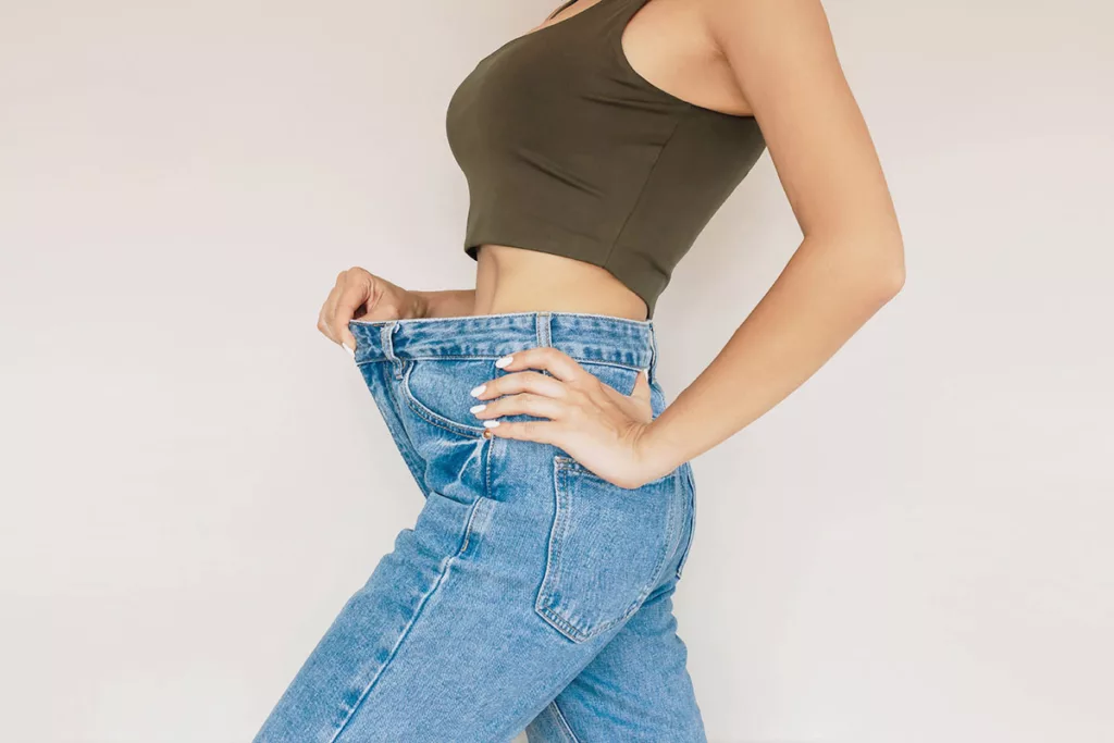 A woman in jeans shows her abdomen after belly fat reduction from body sculpting treatment.