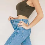 A woman in jeans shows her abdomen after belly fat reduction from body sculpting treatment.