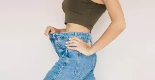 A woman in jeans shows her abdomen after belly fat reduction from body sculpting treatment.