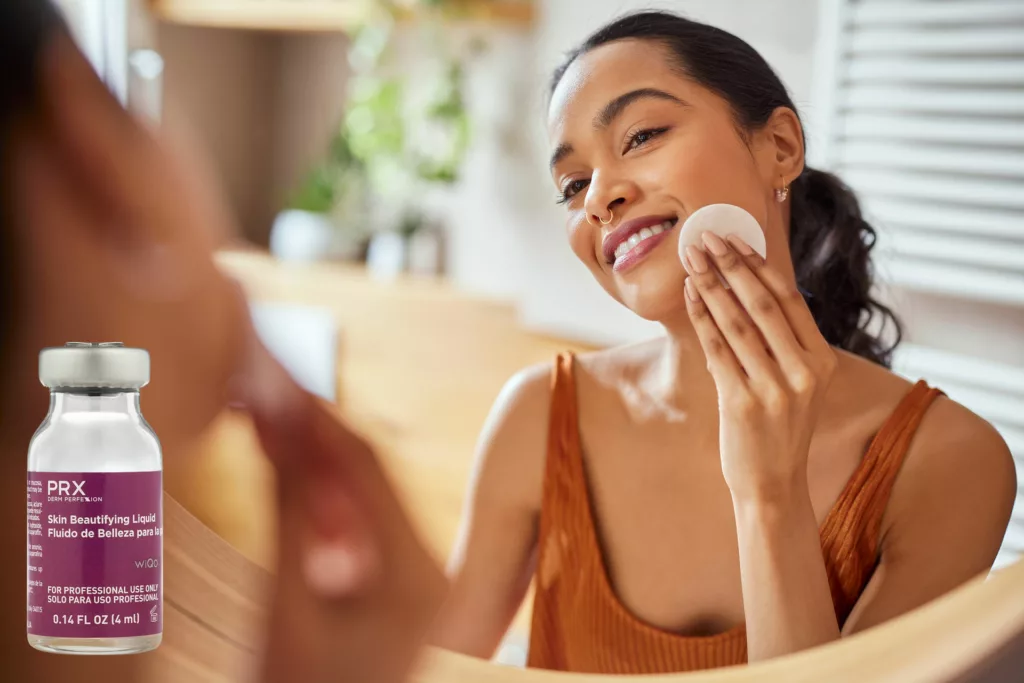 beautiful young woman cleanses her face in the bathroom mirror using a cotton round