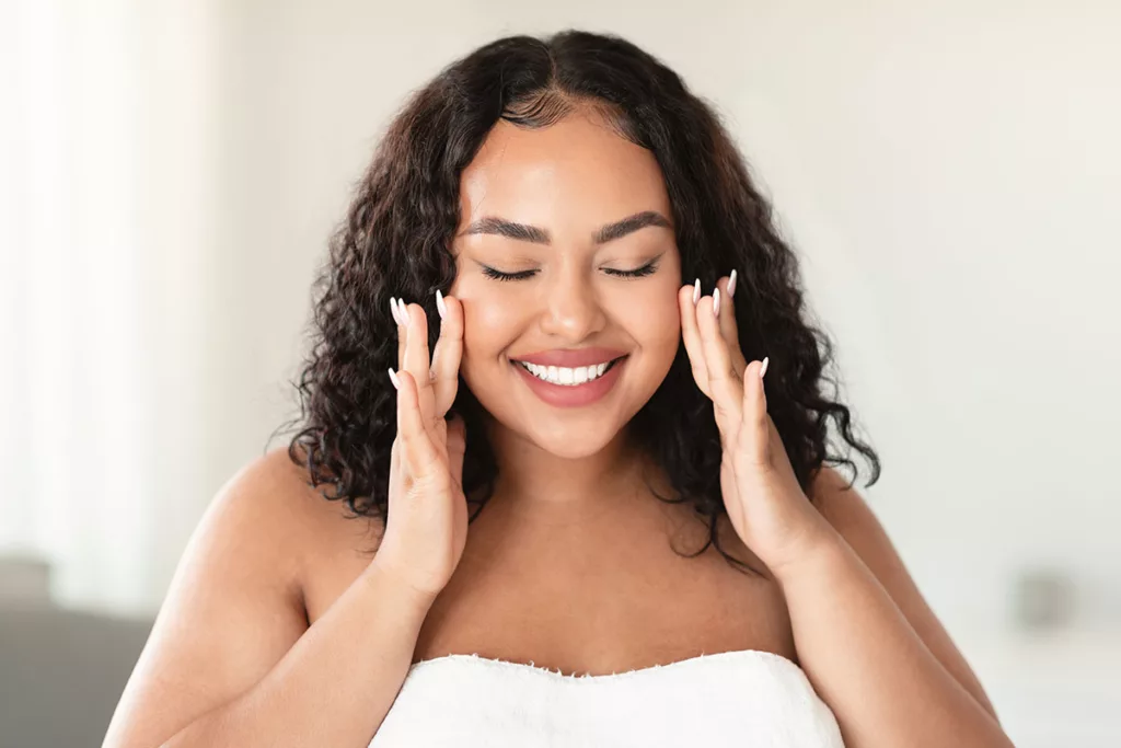 A smiling woman touches her face after a rejuvenating TCA 'no peel' skin treatment.