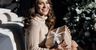 A beautiful woman sitting next to an elegant Christmas tree holiday a present and smiling