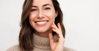 A smiling woman in a brown sweater with glowing skin