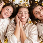 Three beautiful, young, happy women, laying on a bed of gold confetti in spa robes