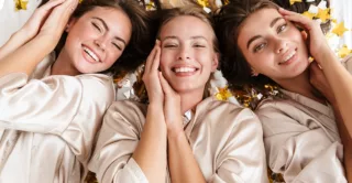 Three beautiful, young, happy women, laying on a bed of gold confetti in spa robes
