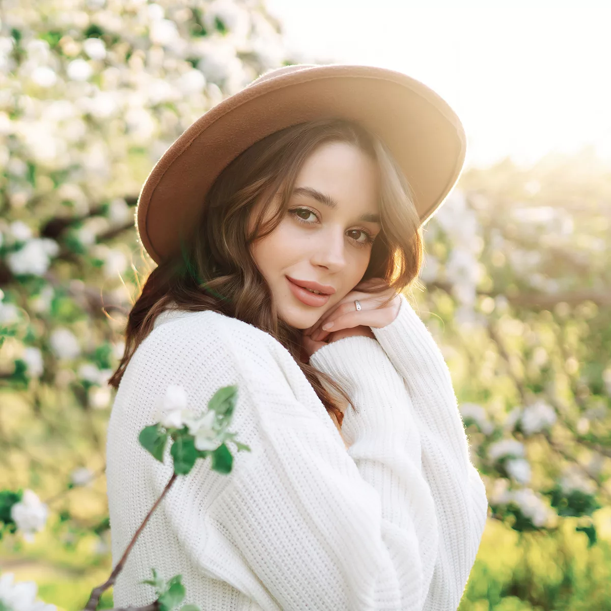 A young woman stands outside by white flowers in spring.