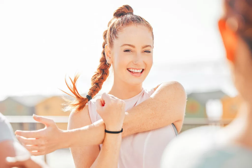young woman stretches her arm muscles while out exercising with friends