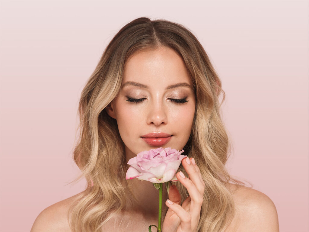 A woman holds a flower against a pink background.
