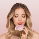 A woman holds a flower against a pink background.