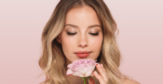 A woman holds a flower against a pink background.