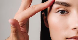 A young woman with smooth skin touches the area around her eye, showing the concept of EMFACE Eye treatment for eye bags and dark circles