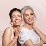 A young woman and her mother standing against a pastel pink background, showing the concept of mother's day