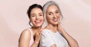 A young woman and her mother standing against a pastel pink background, showing the concept of mother's day