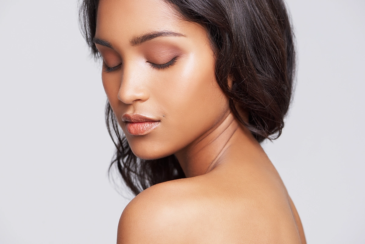 A woman against a light gray background, closing her eyes with smooth skin on her face and neck, showing the concept of Sofwave skin rejuvenation treatments