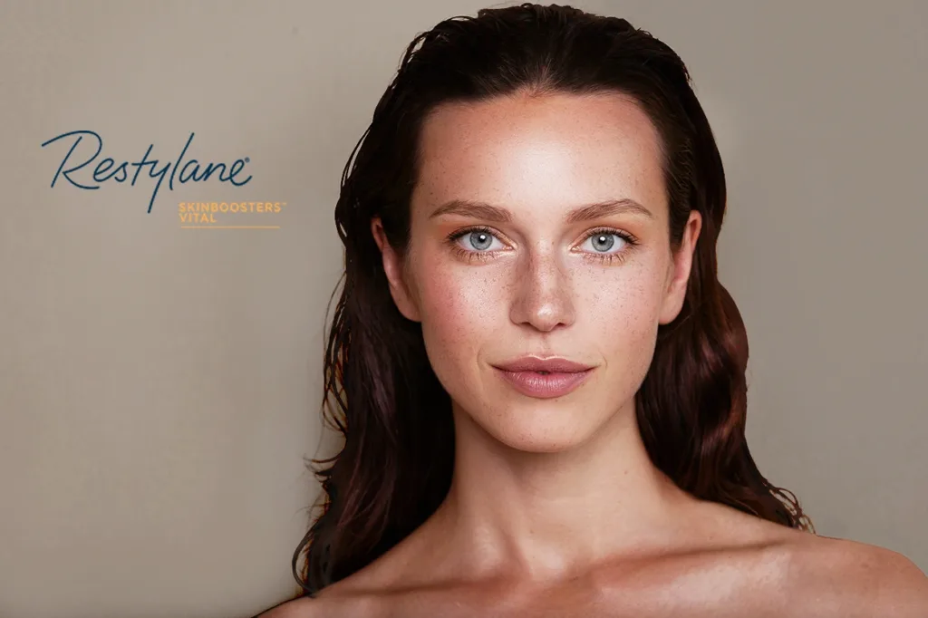 Restylane Skinboosters logo overlay next to a beautiful women with long red-brown hair, blue-grey eyes, and clear, hydrated, healthy, and youthful looking skin.