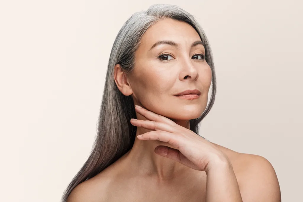 A woman with smooth skin touches her jawline against a light beige background, showing the concept of med spa treatments
