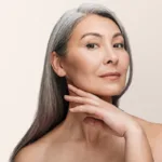 A woman with smooth skin touches her jawline against a light beige background, showing the concept of med spa treatments
