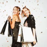 Two smiling women in black dresses holding shopping bags for Black Friday