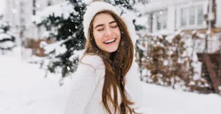 A smiling young woman with long brown hair wearing white winter clothes in the snow