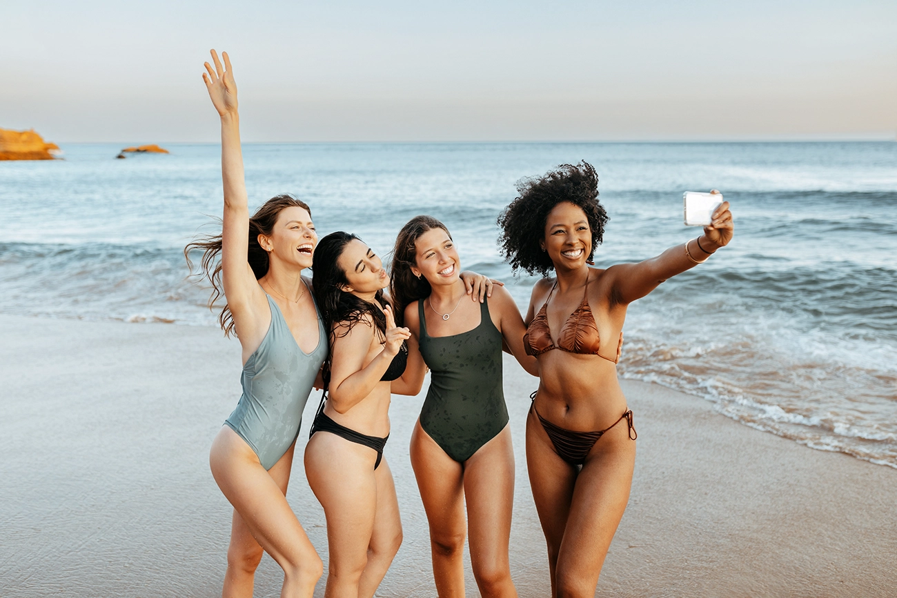 A group of smiling women in swimsuits taking a selfie at the beach