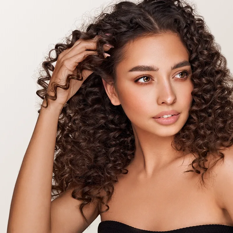 A young woman with clear, healthy skin, nails, and hair against a beige background