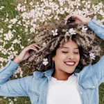A smiling young woman laying in the grass, surrounded by flower petals, showing the concept of spring special offers and promotions