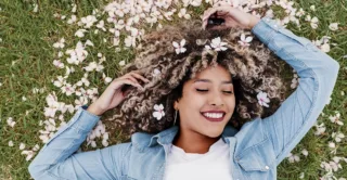 A smiling young woman laying in the grass, surrounded by flower petals, showing the concept of spring special offers and promotions