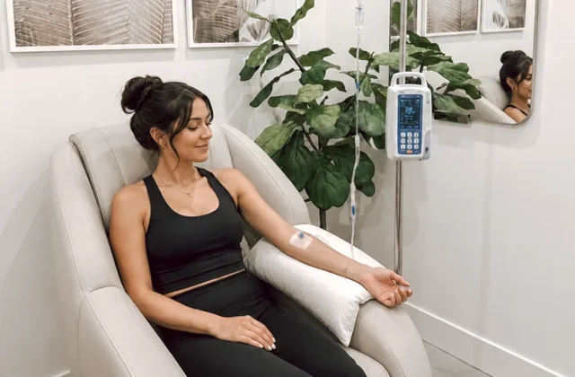 A smiling woman in a med spa clinic receives IV therapy for hydration and wellness, with a ficus plant in the background