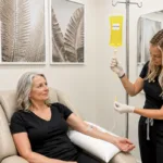A woman receiving IV therapy treatment from a med spa clinic in a lounge chair, with beige walls and tropical art prints in the background