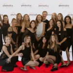 A group photo of the Artemedica team on a red carpet, everyone dressed in black formal wear, next to pillars with flowers